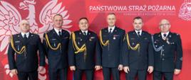 Na zdjęciu znajdują się strażacy ubrani w mundury, w tle znajduje się baner z logo PSP