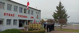 Zdjęcie przedstawia salutujących funkcjonariuszy Państwowej Straży Pożarnej. Fotografia została wykonana przed budynkiem komendy.