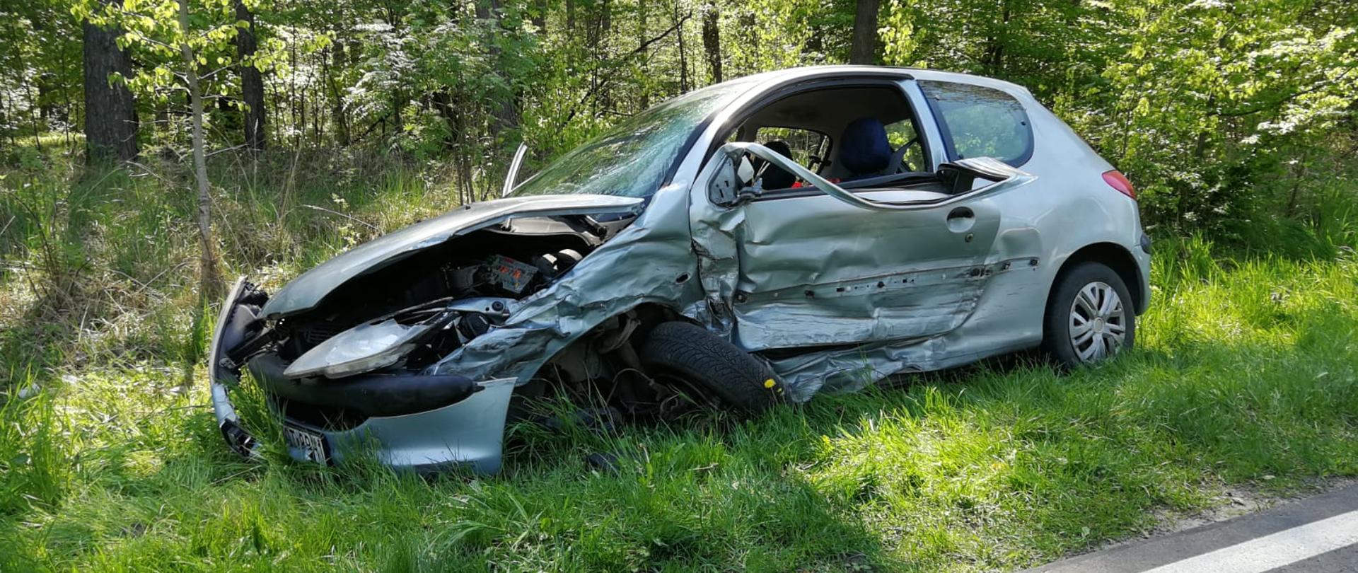 Zdjęcie przedstawia uszkodzony pojazd osobowy, który brał udział w kolizji drogowej. Zdjęcie wykonane na poboczu jezdni w porze dziennej.