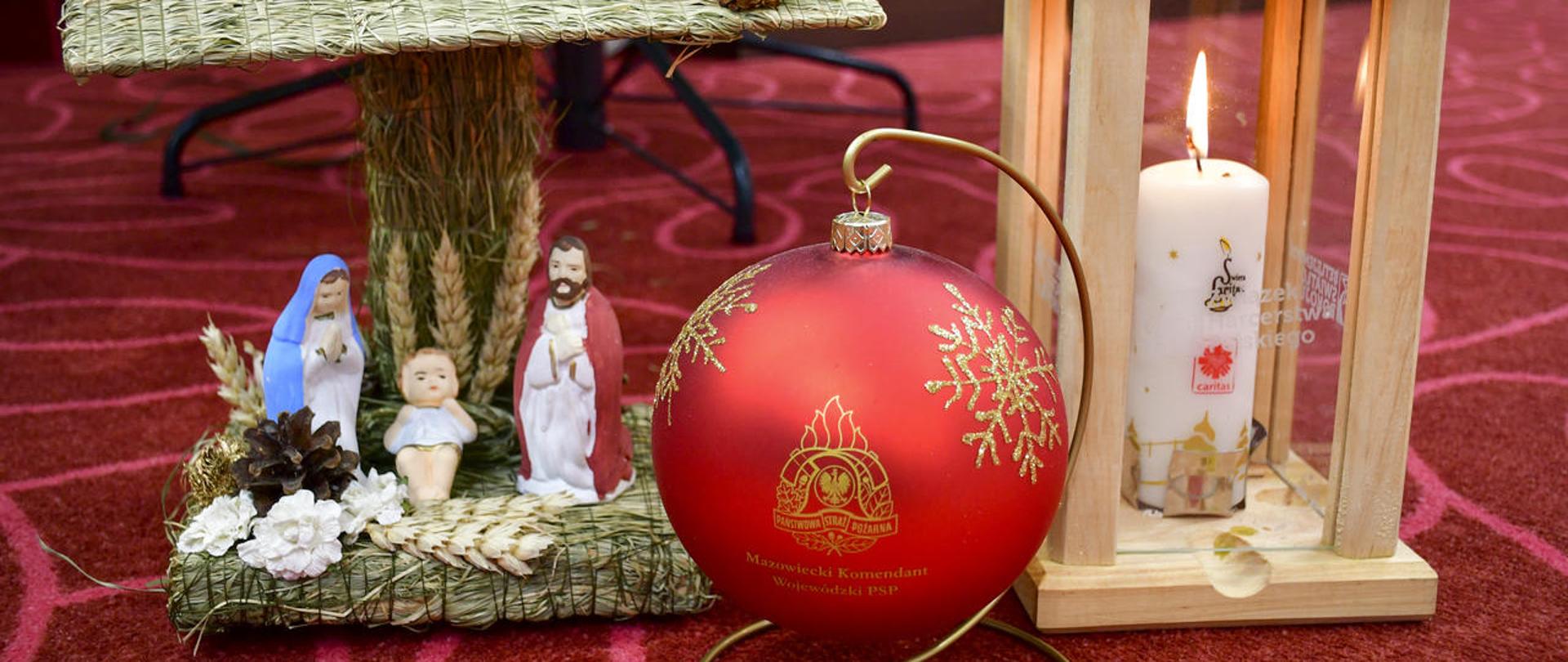 Betlejemskie Światełko Pokoju stoi obok bombki i szopki bożonarodzeniowej.