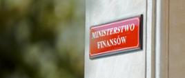 Czerwona tablica z napisem „MINISTERSTWO FINANSÓW” na elewacji budynku.