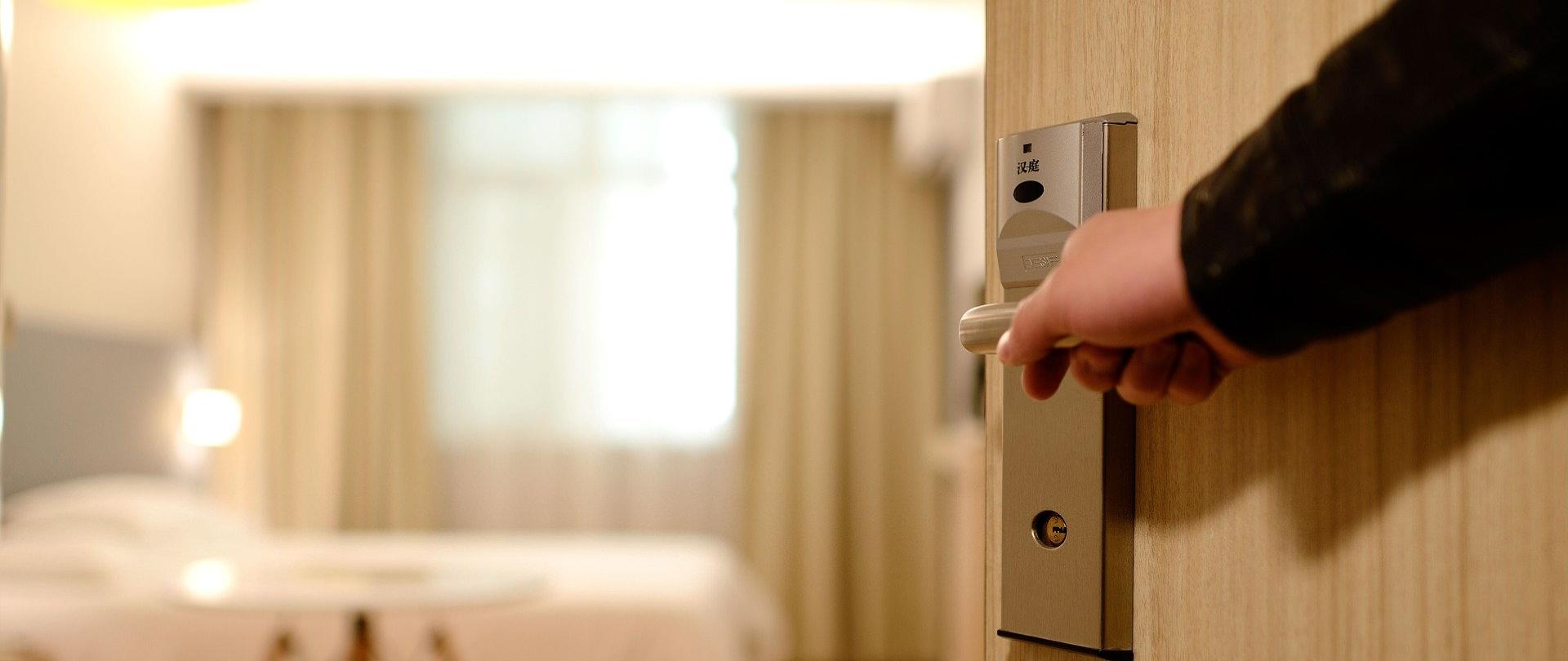 ręka na klamce drzwi otwierających pokój hotelowy