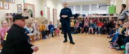 Na zdjęciu znajdują się dzieci oraz strażak ubrany w ubiór służbowy i policjantka, w sali podczas pogadanki