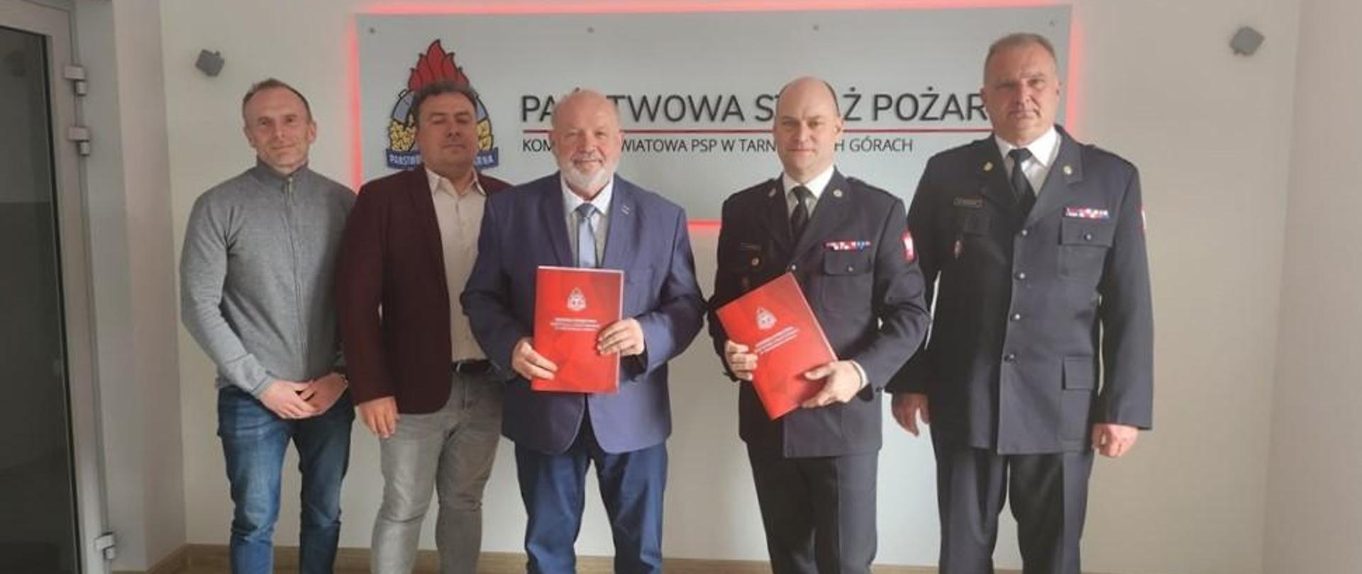 Pięciu mężczyzn stoi w rzędzie. dwóch trzyma w ręku czerwone teczki.