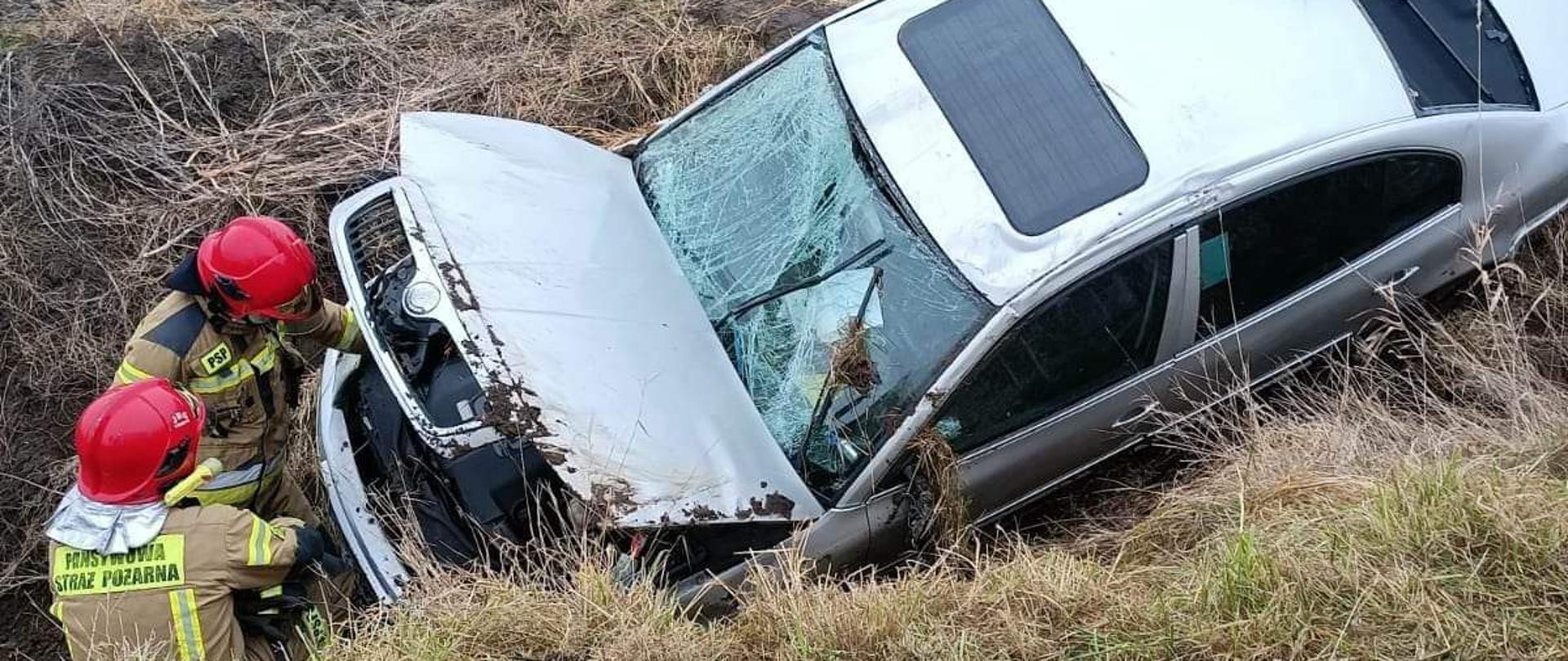 Samochód osobowy znajduje się w rowie przy nim dwaj strażacy