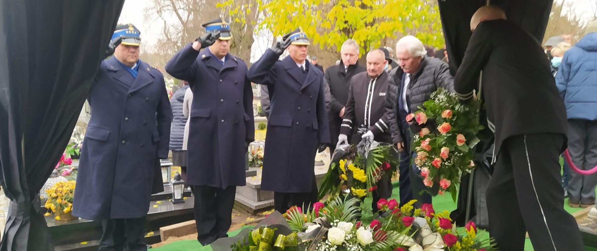 Pogrzeb strażaka. Cmentarz parafialny w Łaszczynie. Przed grobem zmarłego strażaka delegacja strażaków po złożeniu wiązek kwiatów oddaje honor swojemu zmarłemu koledze. 