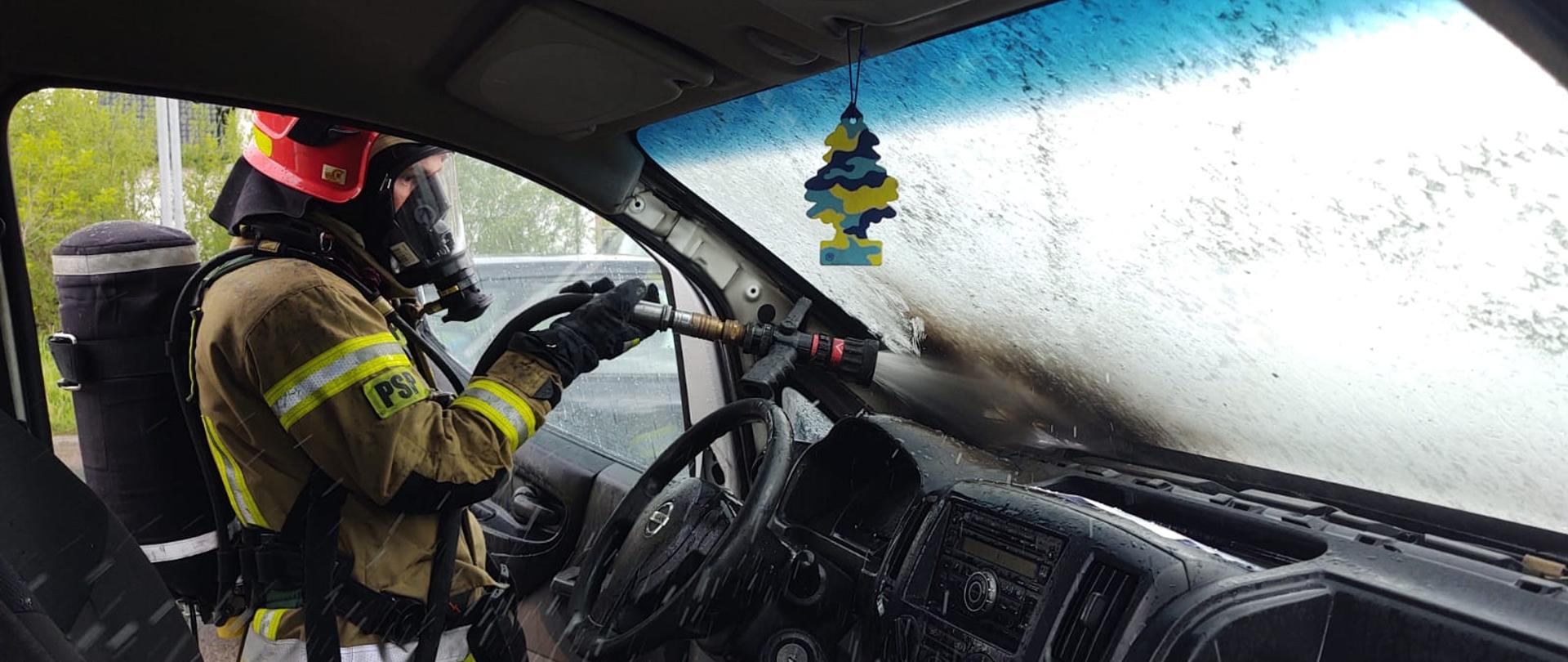 Strażak podaje prąd wody do wnętrza pojazdu.