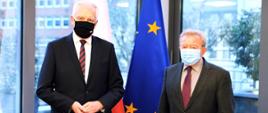 Wicepremier, minister rozwoju, pracy i technologii Jarosław Gowin w maseczce na twarzy, po jego prawej stronie stoi komisarz UE ds. rolnictwa Janusz Wojciechowski. Z tyłu flagi Polski i UE.