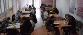 Przy stolikach, ustawionych w dwa rzędy, siedzą dzieci i młodzież i rozwiązuje testy.