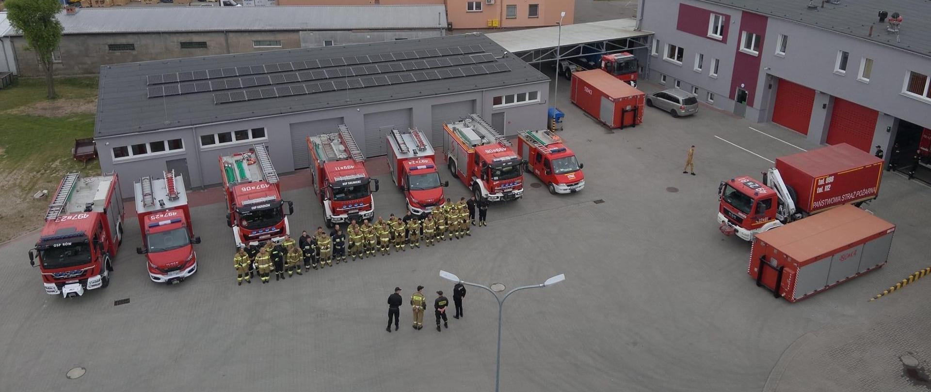 Zdjęcie przedstawia pojazdy pożarnicze oraz strażaków PSP i OSP na zbiórce przed ćwiczeniami gminnymi