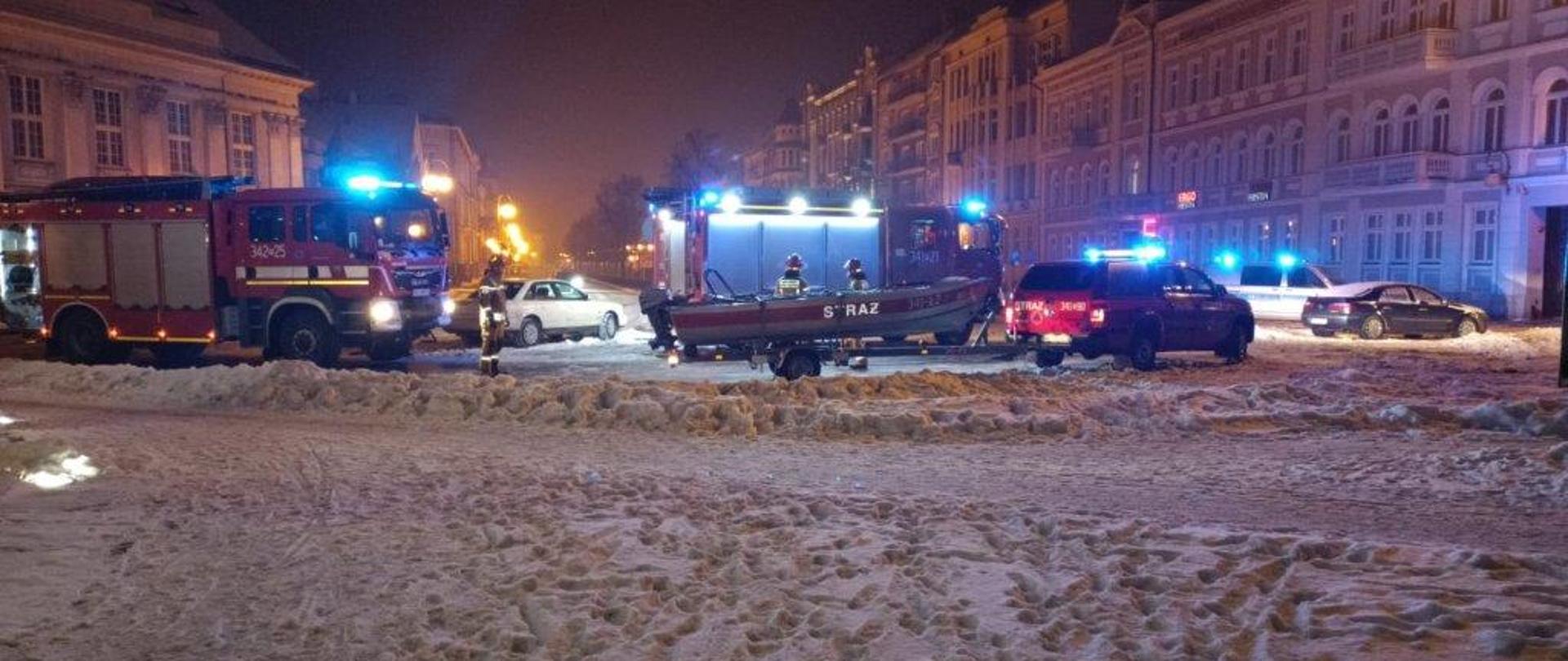 pojazdy straży pożarnej na sygnałach świetlnych i łódź stoją na ulicy pokrytej śniegiem 