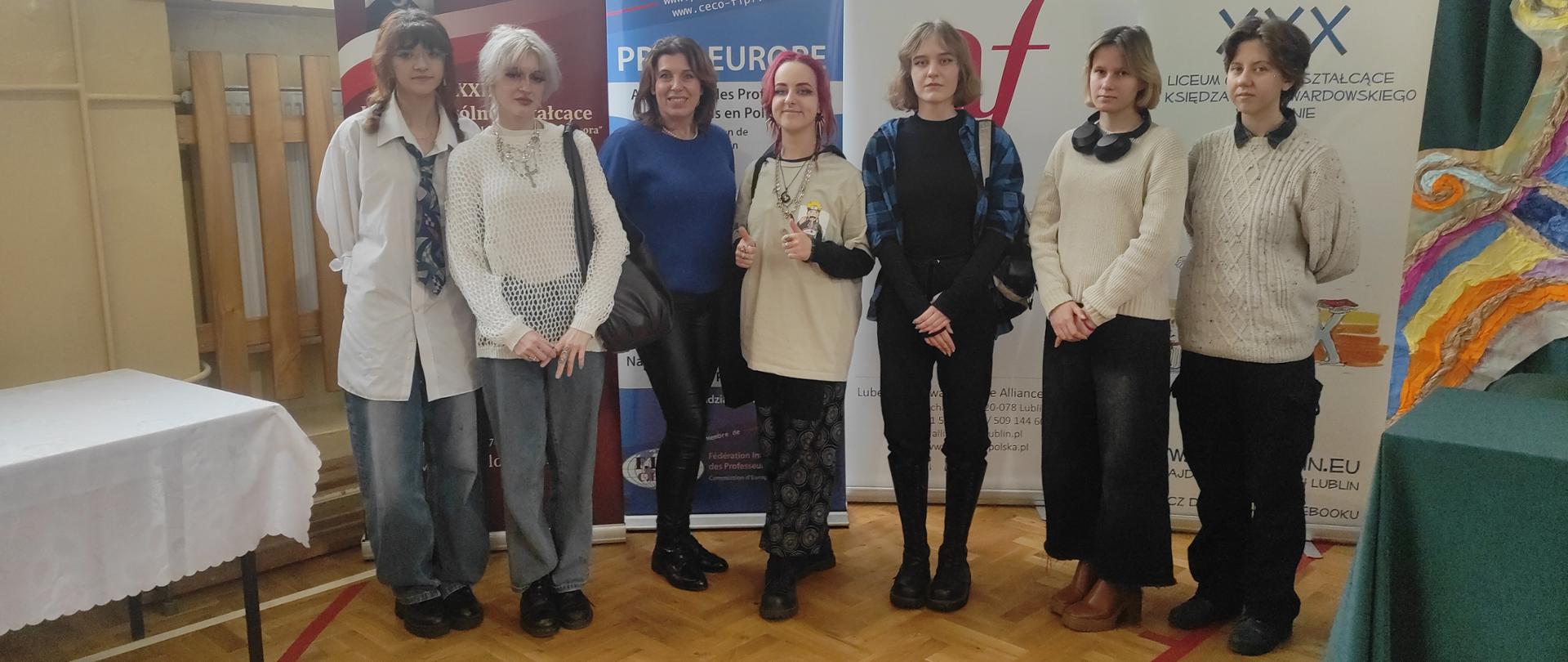 Zdjęcie grupowe, pozowane. Uczennice PLSP w Lublinie i nauczycielka stoją w sali budynku XXIX LO w Lublinie. W tle wiszą różne plakaty.