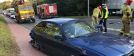 Samochód osobowy BMW z uszkodzonym tyłem w tle strażacy i policja