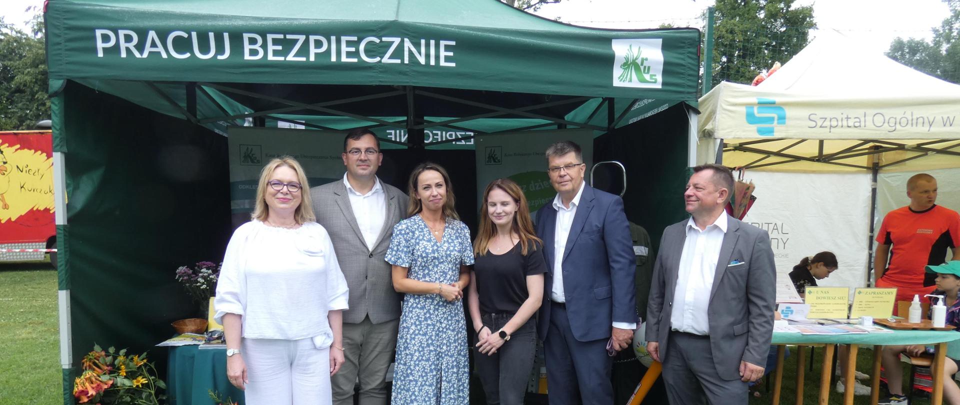 Trzy kobiety i trzech mężczyzn stoją przed namiotem ze stoiskiem informacyjnym KRUS.
