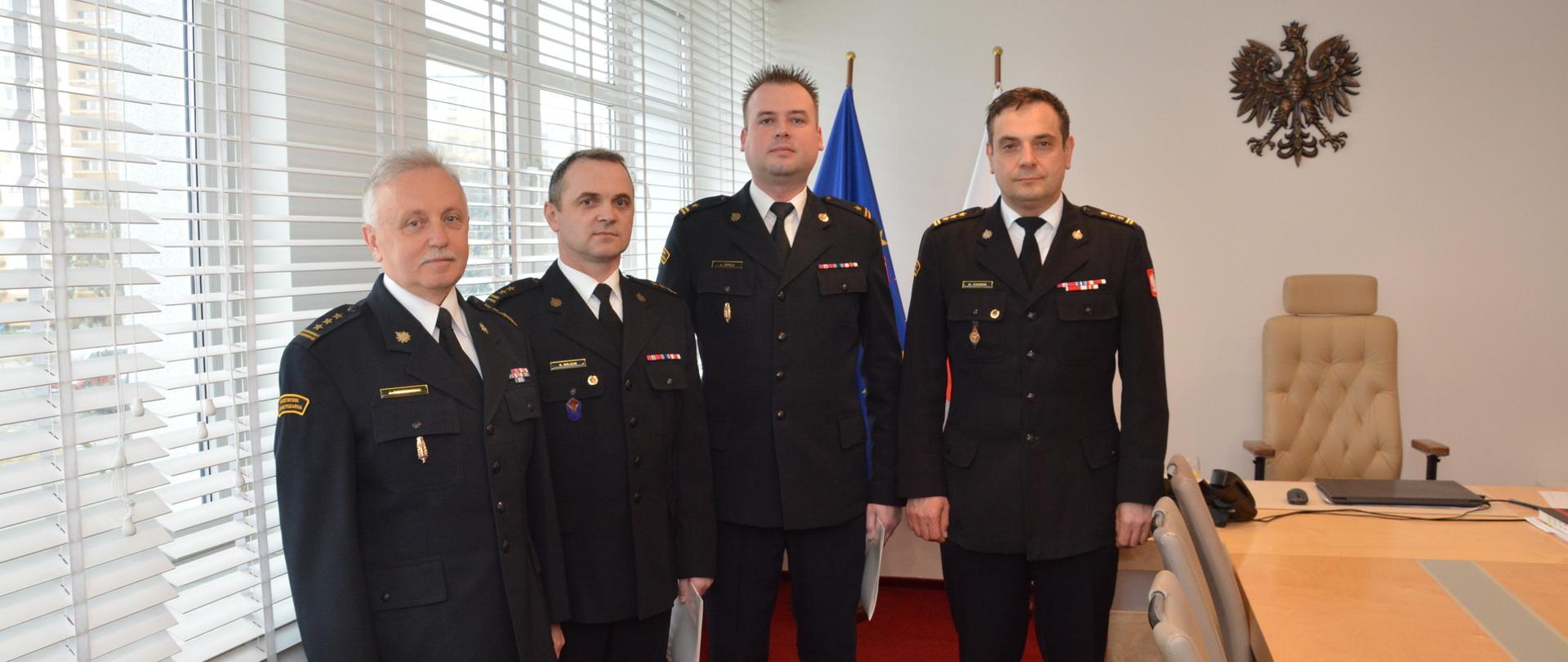 Na pierwszym planie widzimy czterech mężczyzn w umundurowaniu wyjściowym w gabinecie na tle flag: Polski i Unii Europejskiej. 