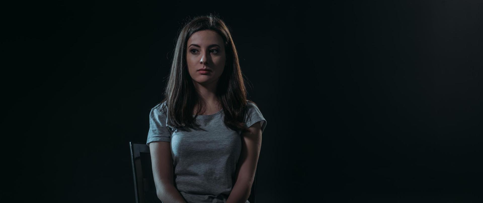 Na zdjęciu jest kobieta siedząca na krześle. Tło jest czarne.