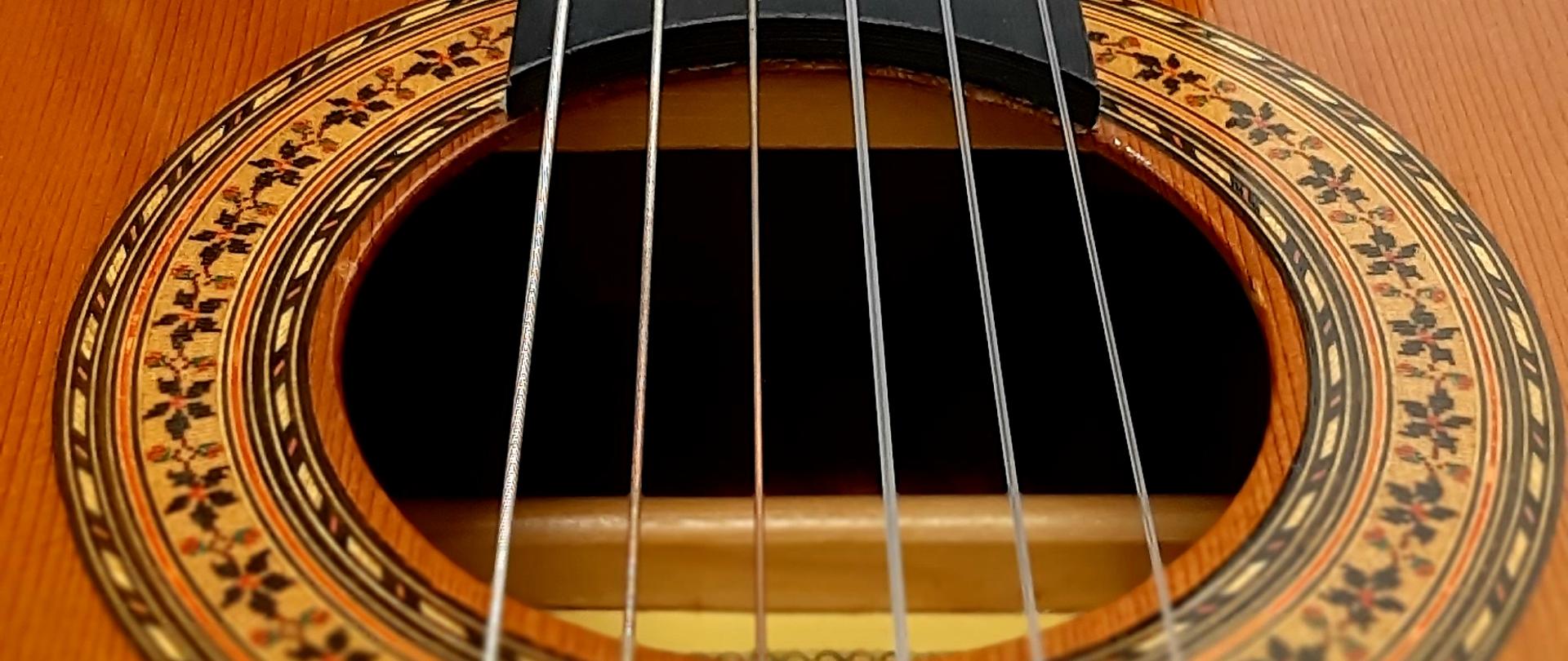 Zdjęcie przedstawia struny gitary i fragment pudła wraz z gryfem