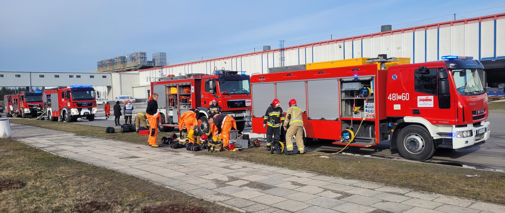 Ratownicy przygotowujący się do działań ratowniczych, w tle pojazdy ratownicze