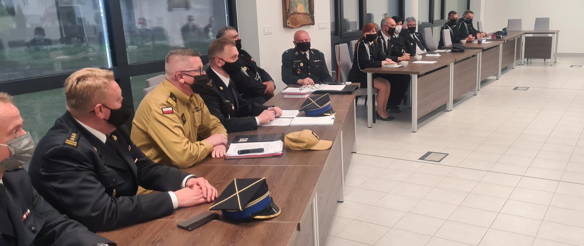 Na zdjęciu widać 4 strażaków i 7 druhów w mundurach galowych siedzących przy stale w trakcie narady