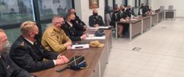 Na zdjęciu widać 4 strażaków i 7 druhów w mundurach galowych siedzących przy stale w trakcie narady