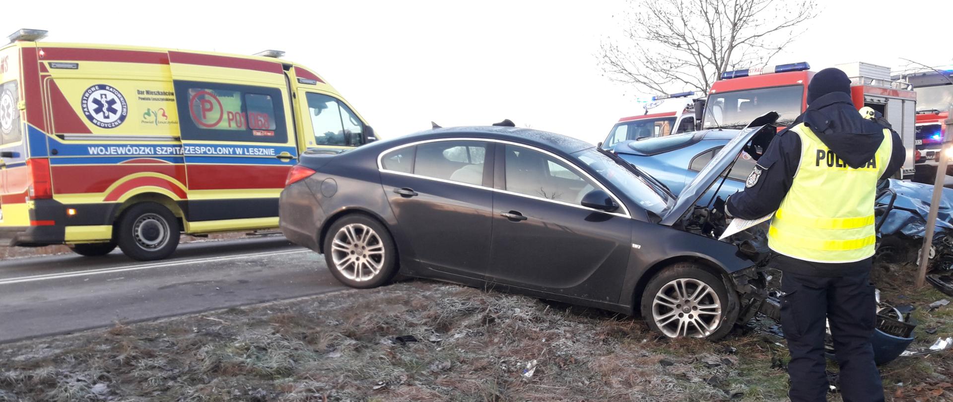 SAMOCHÓD PO WYPADKU, W TLE KARETKA, NA PIERWSZYM PLANIE POLICJANT
