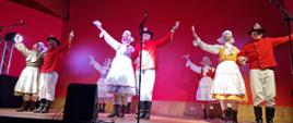 Un groupe de musiciens en costumes folkloriques polonais danse sur scène.