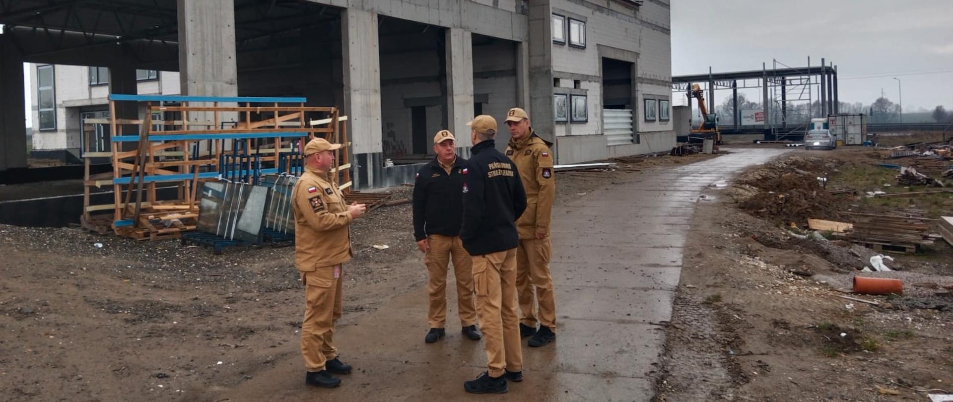 Funkcjonariusze Państwowej Straży Pożarnej na placu budowy. W tle budynek w trakcie budowy.