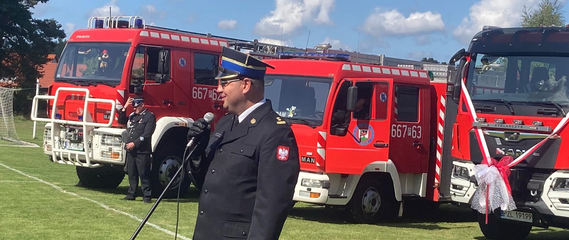 zastępca wielkopolskiego komendanta wojewódzkiego PSP przemawia do uczestników wydarzenia, w tle samochody strażackie