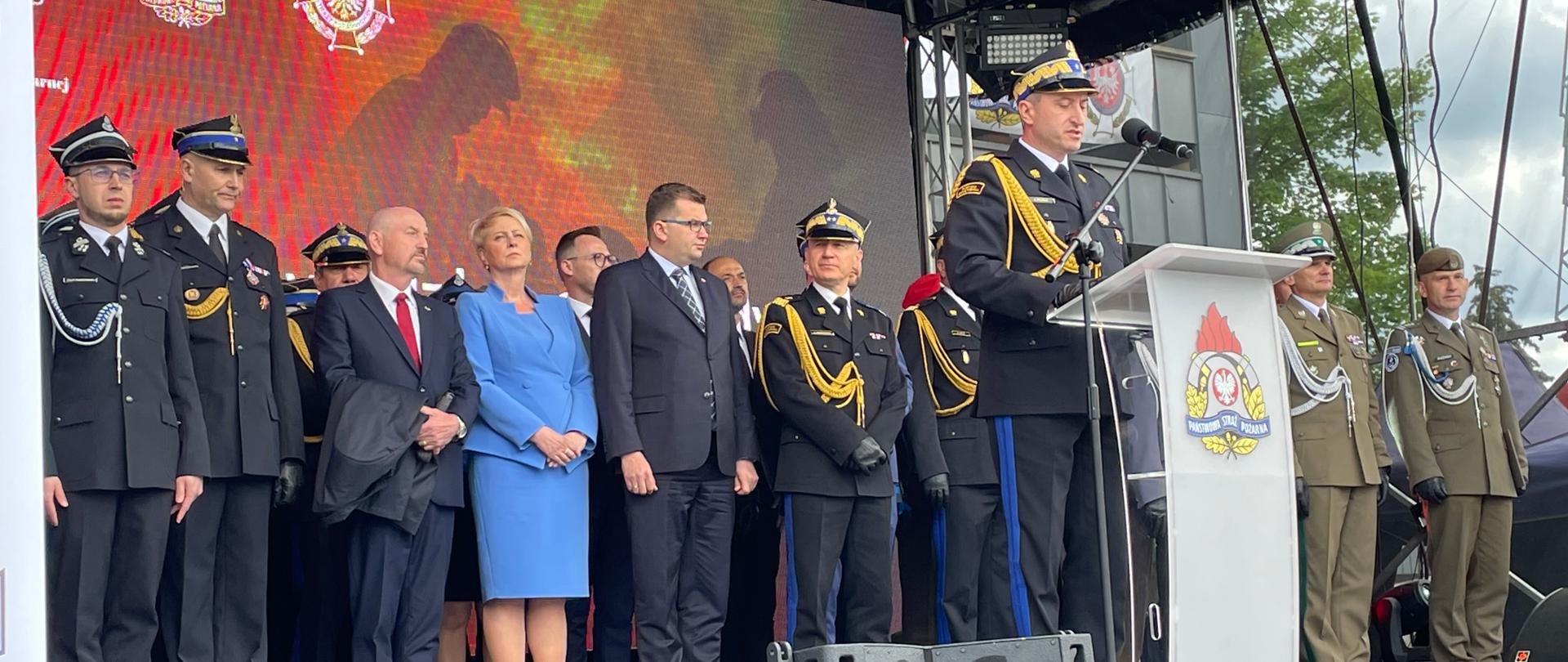 Małopolski KW PSP przemawia na trybunie honorowej. Za nim stoją zaproszeni goście