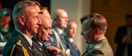 Komendant Centralnej Szkoły PSP w Częstochowie podczas uroczystej gali odbiera Medal za Zasługi dla Straży Granicznej od oficera w stopniu generała brygadera Straży Granicznej. W tle widoczni są przedstawiciele służb mundurowych uczestniczący w ceremonii