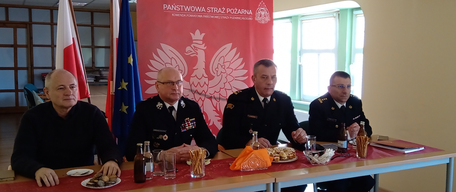 Sala konferencyjna. Przy stole sidzą od prawej strony: Zastępca Komendanta Powiatowego PSP w Kłodzku, Komendant Powiatowy PSP w Kłodzku, Prezes Zarządu Ochotniczych Straży Pożarnych RP powiatu kłodzkiego oraz Dyrektor Wydziału Zarządzania Bezpieczeństwa
Kryzysowego i Polityki Zdrowotnej Starostwa Powiatowego w Kłodzku.
