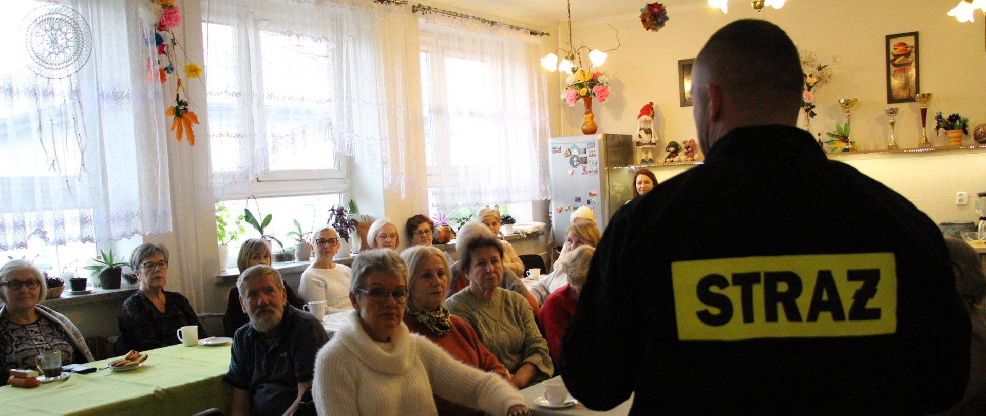 Zdjęcie przedstawia strażak, który prowadzi prelekcję w klubie seniora.