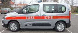 Nowy samochód specjalny. Plac Komendy Powiatowej PSP w Rawiczu, na którym zaparkowany jest nowy nabytek - lekki samochód kwatermistrzowski. Auto ma srebrny kolor. Na karoserii naklejony jest czerwony pas, na którym znajduje się napis STRAŻ oraz numer 571P81. Widok z boku, od strony kierowcy.