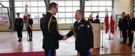 Zastępca KG PSP podaje rękę w geście podziękowań lubuskiemu KW PSP, w tle strazacy i osoby cywilne podczas uroczystoisci w hali garażowej