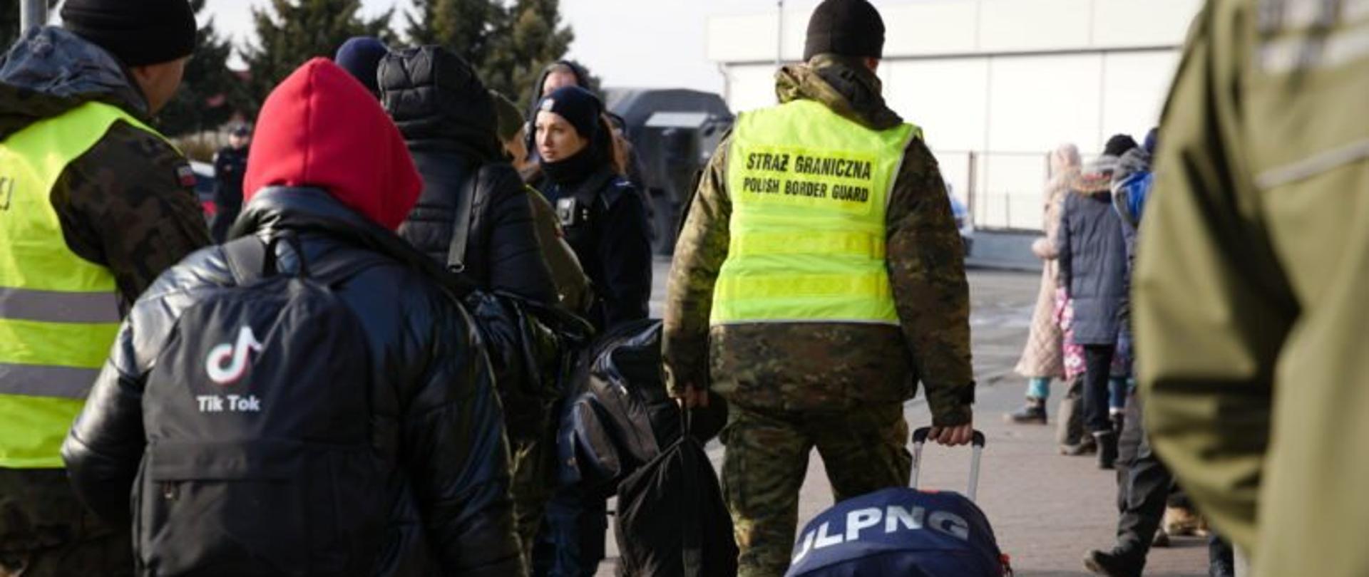 Funkcjonariusz Straży granicznej pomagają uchodźcom z Ukrainy w niesieniu bagażu