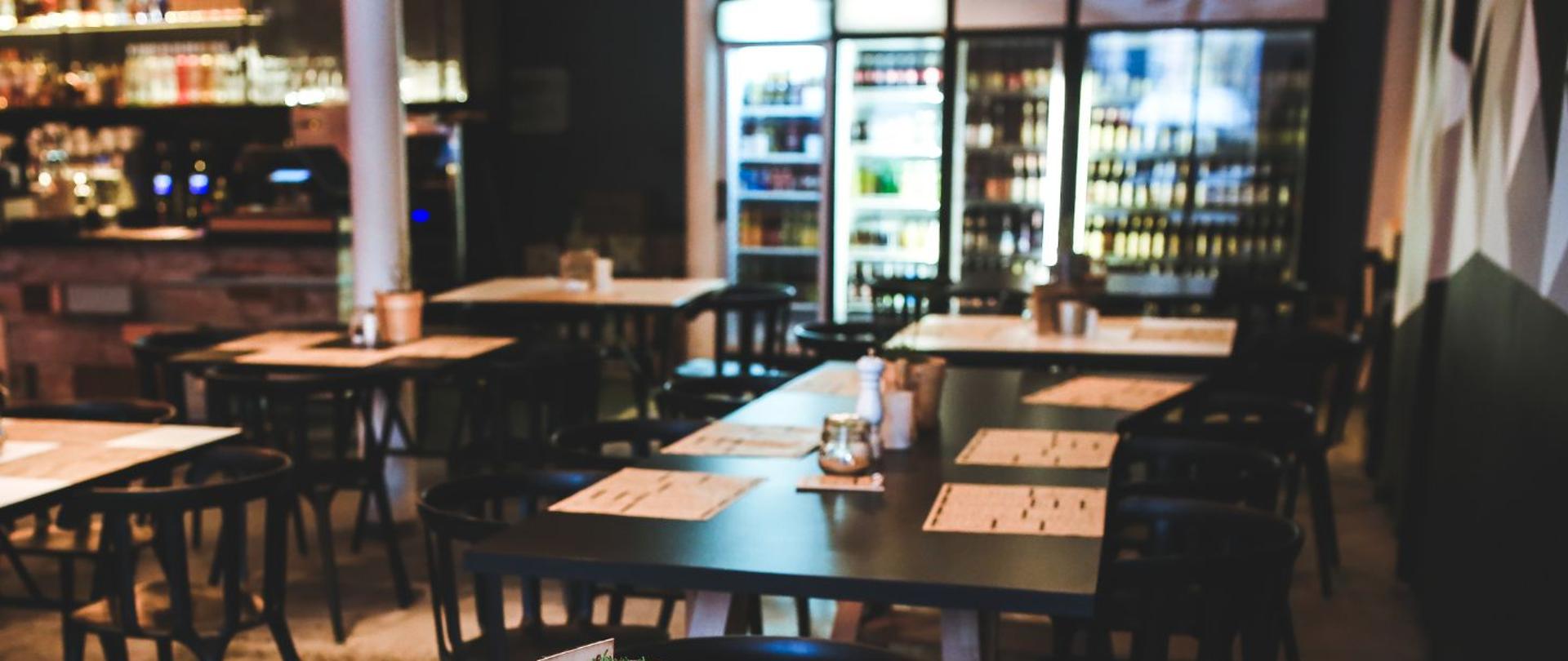 na zdjęciu widoczne są stoliki w restauracji, na tylnym planie widać lodówki z napojami. 