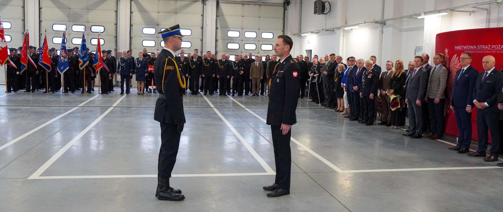 Część oficjalna obchodów Powiatowego Dnia Strażaka na garażu Komendy Powiatowej Państwowej Straży Pożarnej w Opocznie. Przyjęcie meldunku Łódzkiego Komendanta Wojewódzkiego od dowódcy. W tle zaproszeni goście oraz poczty sztandarowe. 