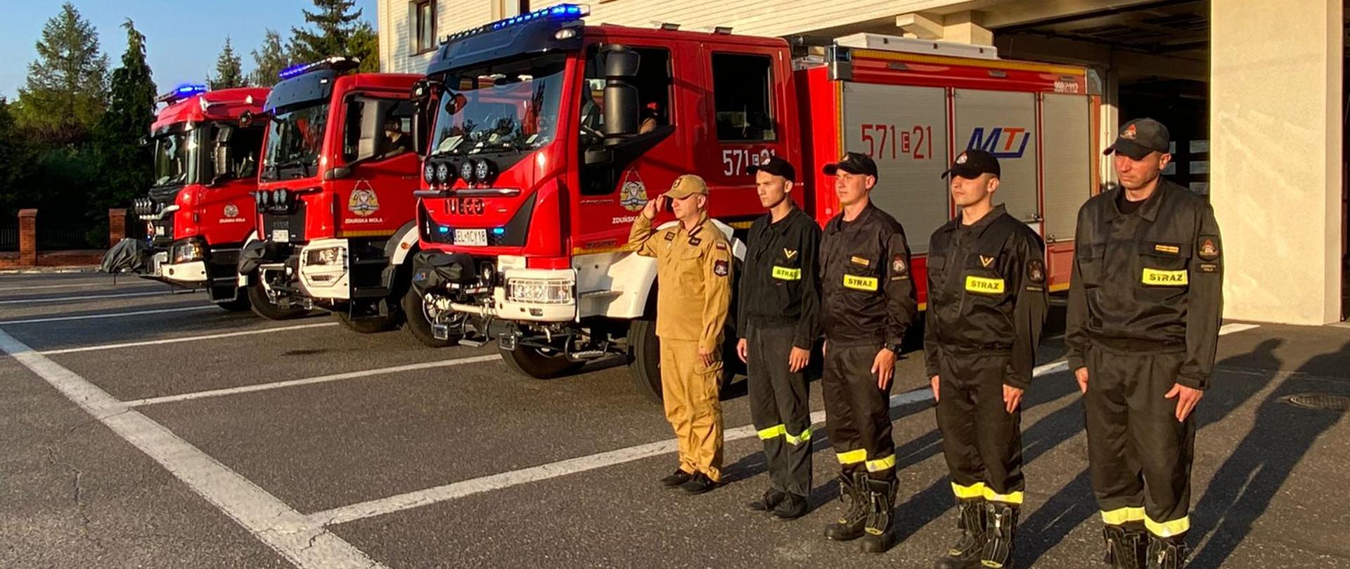 Przed budynkiem Komendy Powiatowej PSP w Zduńskiej Woli wystawione są pojazdy pożarnicze które mają włączone sygnały świetlne oraz dźwiękowe. Przy pojazdach zduńskowolscy strażacy zmiany służbowej drugiej, oddają hołd zmarłemu druhowi Markowi Bartwickiemu.