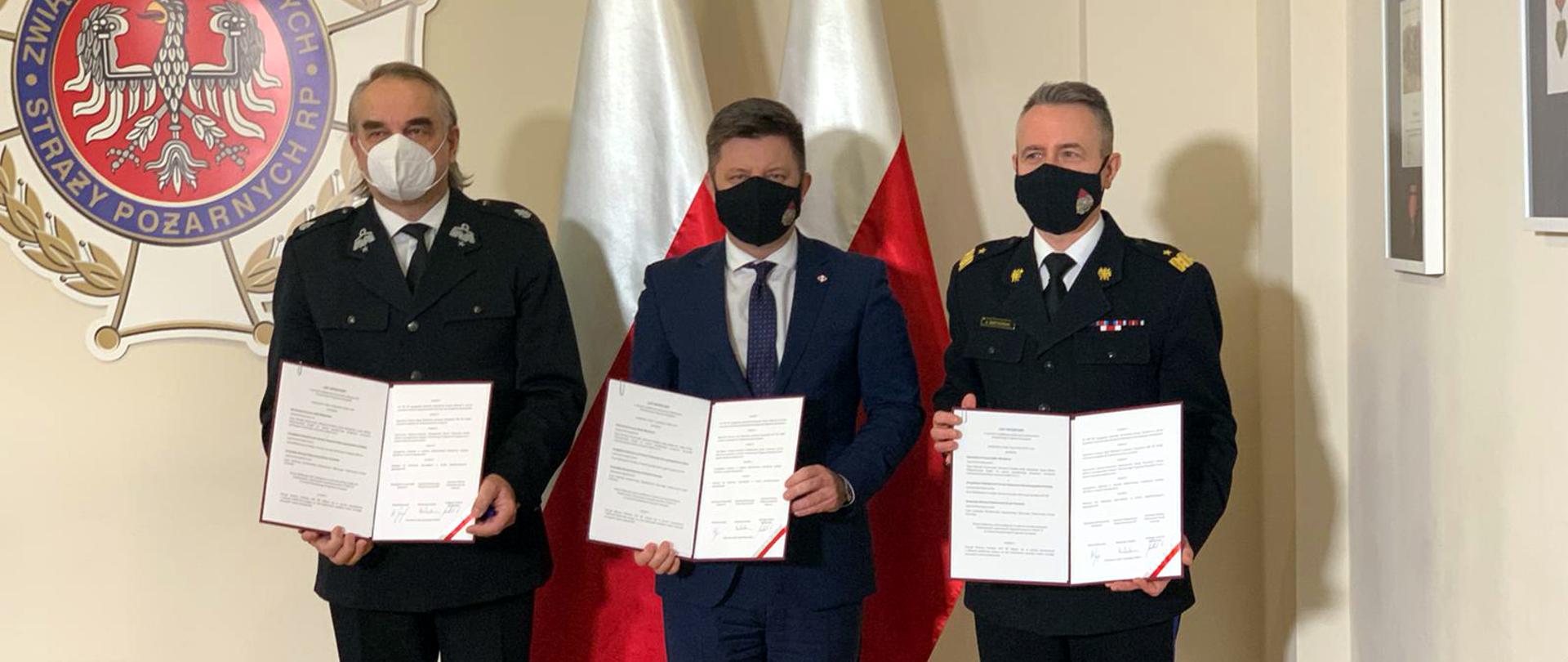 Siedziba Zarządu Głównego Związku Ochotniczych Straży Pożarnych Rzeczypospolitej Polskiej, stoją Michał Dworczyk, szef Kancelarii Prezesa Rady Ministrów z nadbryg. Andrzejem Bartkowiakiem, komendantem głównym PSP i dh. Waldemarem Pawlakiem prezesem ZG ZOSP RP. Wszyscy trzymają podpisany list intencyjny. 