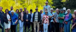 Grupa osób, w tym wicewojewoda, pozują do wspólnego zdjęcia na tle lasu oraz zabudowań Studium Leśnego.