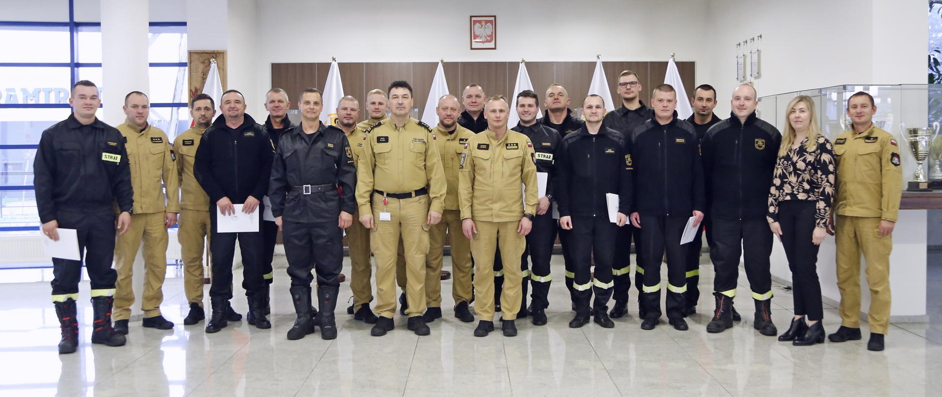 Grupowe zdjęcie funkcjonariuszy PSP uczestniczących w szkoleniu (12 osób) w towarzystwie Komendanta Centralnej Szkoły PSP, Zastępcy Komendanta Centralnej Szkoły PSP, sześciu funkcjonariuszy CS PSP oraz kobiety