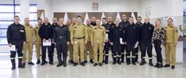Grupowe zdjęcie funkcjonariuszy PSP uczestniczących w szkoleniu (12 osób) w towarzystwie Komendanta Centralnej Szkoły PSP, Zastępcy Komendanta Centralnej Szkoły PSP, sześciu funkcjonariuszy CS PSP oraz kobiety