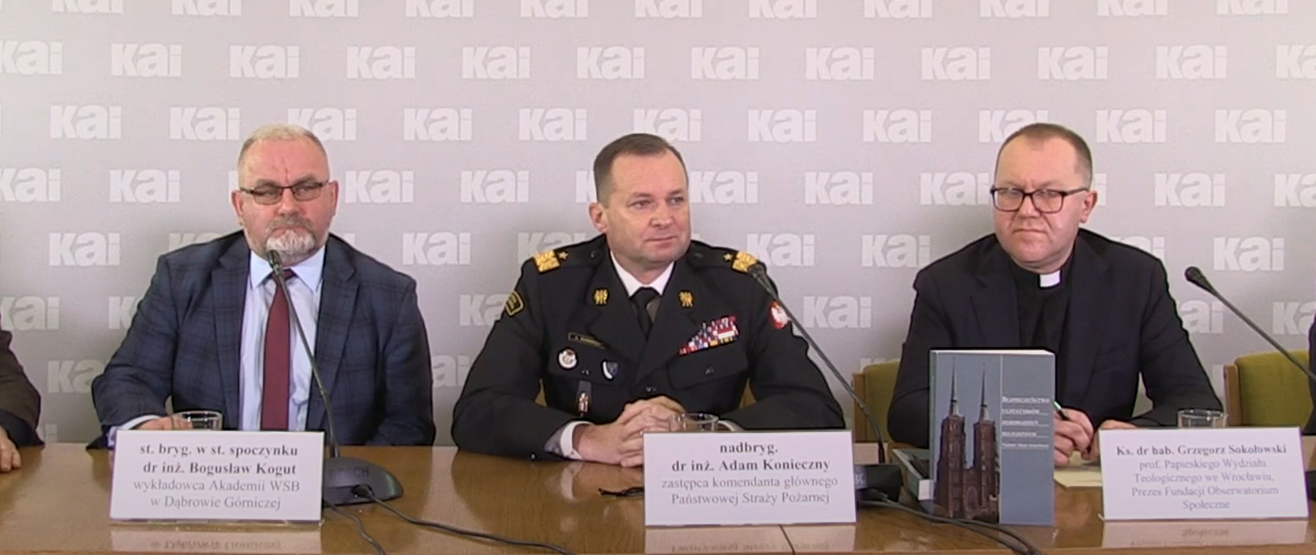 Na zdjęciu widać pięciu uczestników, którzy siedzą za stołem prezydialnym, podczas konferencji prasowej "Bezpieczeństwo uczestników zgromadzeń religijnych"