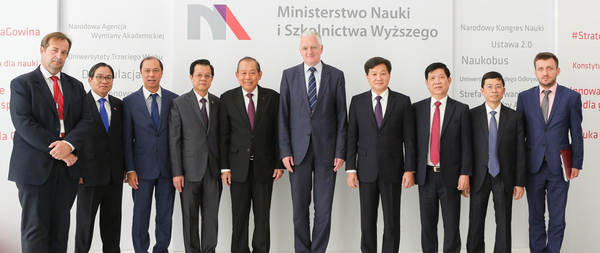 Na tle ściany z logiem MNiSW stoi minister Gowin w otoczeniu delegacji wietnamskiej