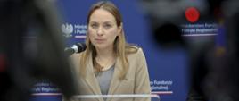 Minister funduszy i polityki regionalnej Katarzyna Pełczyńska-Nałęcz stoi przy mikrofonie, za jej plecami ścianka z logo MFiPR