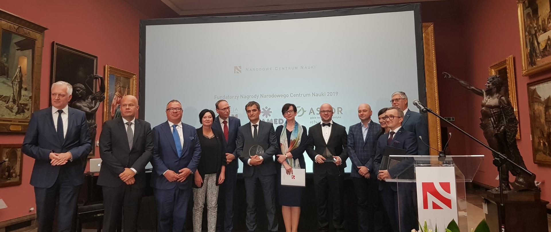 Laureaci nagród i zgromadzeni goście stoją na scenie