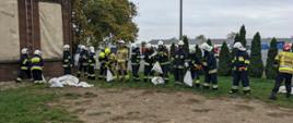 Słuchacze Szkolenia Podstawowego Strażaków Ratowników OSP podczas zajęć praktycznych z tematyki przeciwpowodziowej. Nasypują piach do worków i korzystając z odpowiedniej techniki tworzą z nich wał.