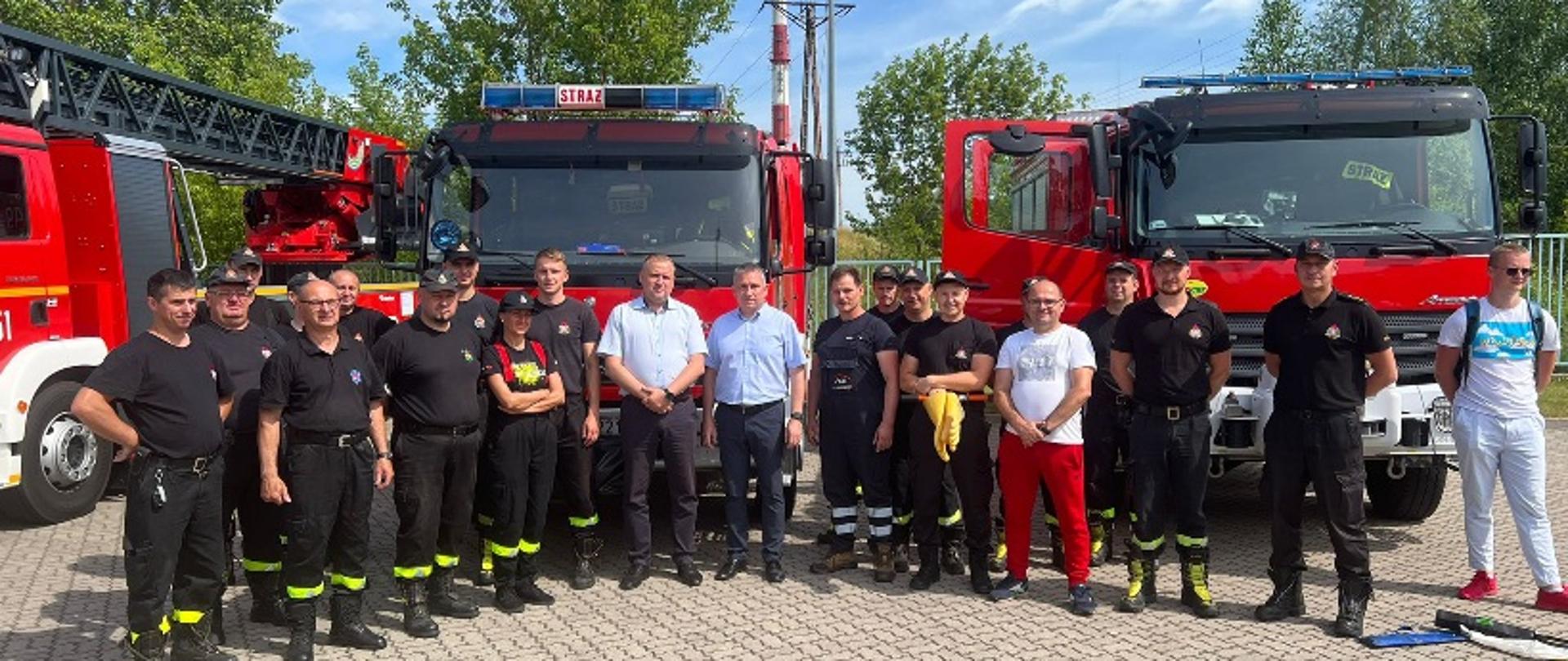 Pracownicy zakładu i funkcjonariusze na tle wozów bo strażackich