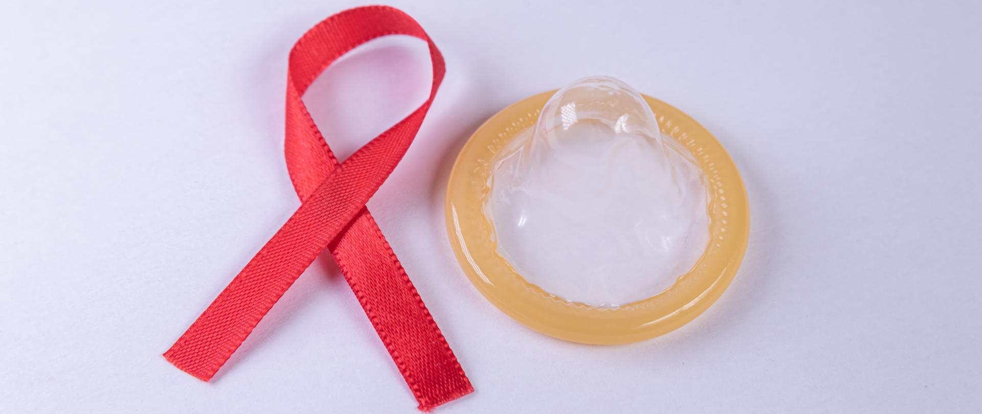 Zdjęcie przedstawia czerwoną kokardkę- symbol AIDS i prezerwatywę, jako jedną z metod profilaktyki zakażeń HIV