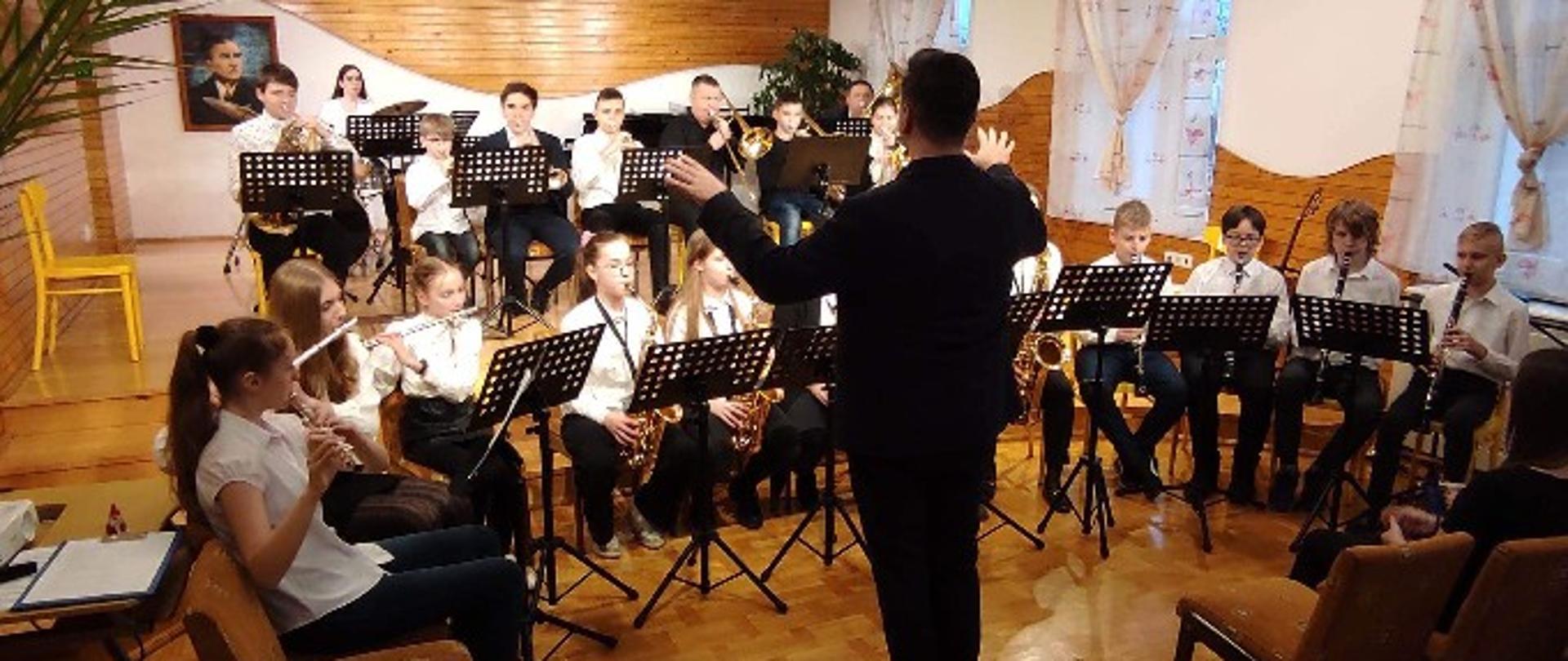zdjęcie przedstawiające uczniów i dyrygenta orkiestry szkolnej na scenie